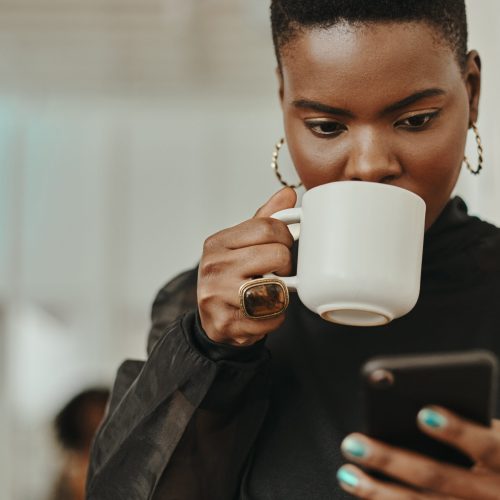 Shot of a young businesswoman having coffee and using a smartphone in a modern office